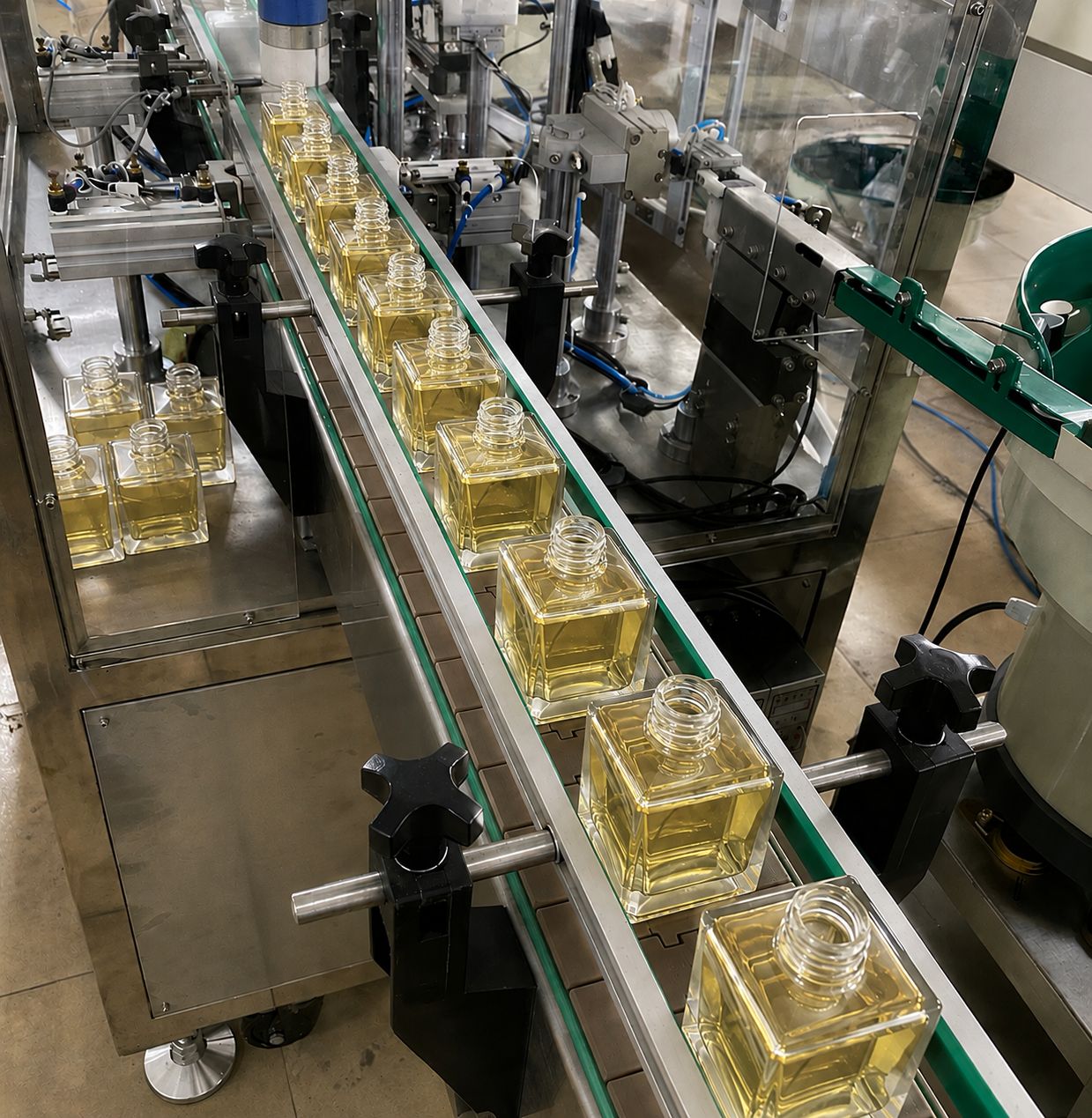 Square glass bottles of yellow fragrance oil on a high-speed filling line